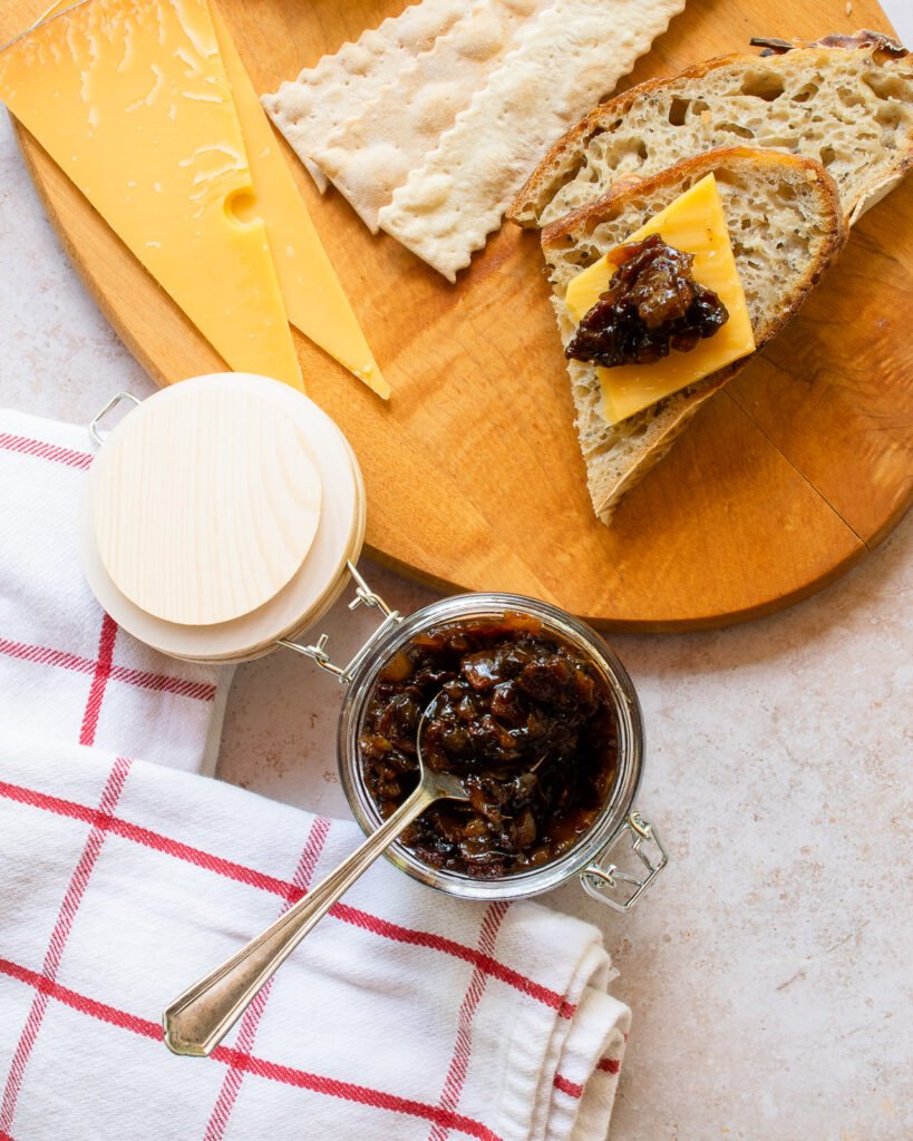 Bacon jam in a jar with a spoon sticking out of it and a piece of bread with cheese and bacon jam.