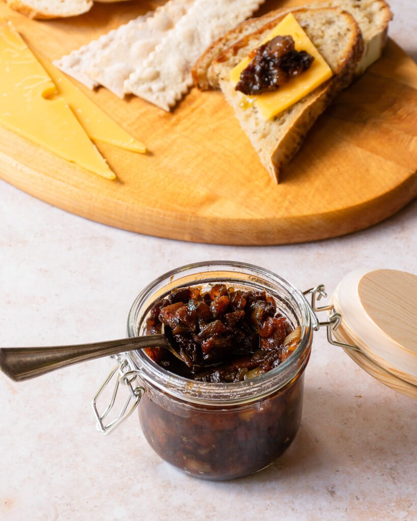A jar of bacon jam with a cheese board in the background.