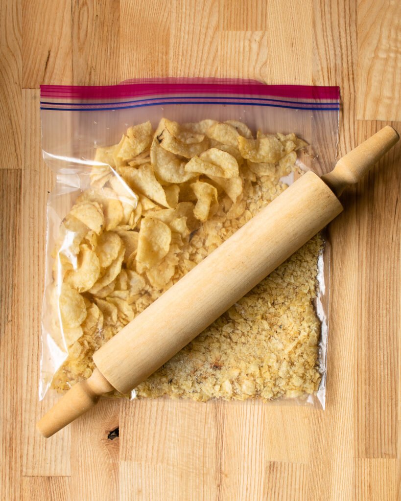 Potato chips in a ziplock bag with a rolling pin crushing them into crumbs.