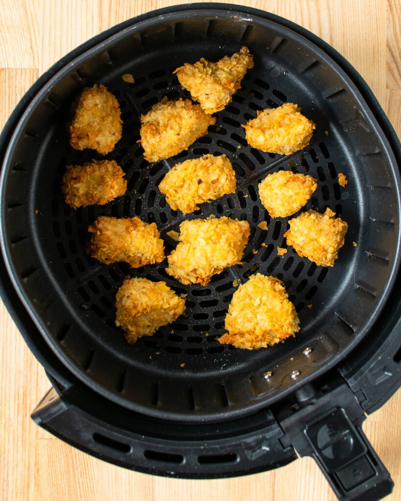 Chip crusted chicken nuggets in the basket of an air fryer.