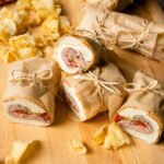 Roast beef sandwiches wrapped in parchment paper on a cutting board with chips scattered around.