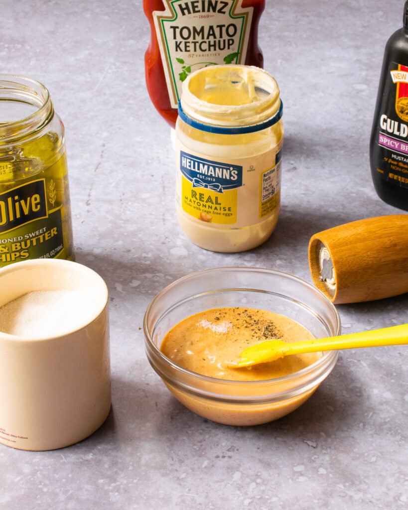 A bowl of burger sauce surrounded by its ingredients - ketchup, mayo, mustard, pickles, salt and pepper.