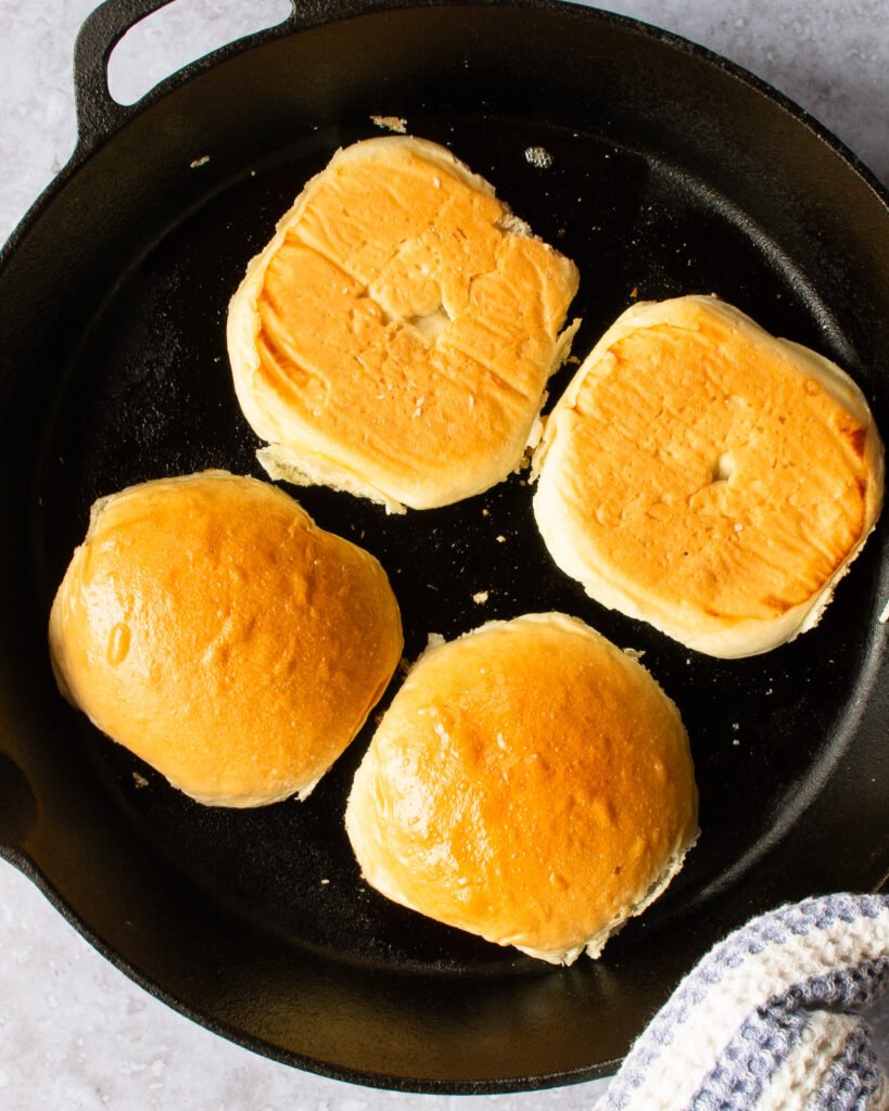 Two halved hamburger buns toasting in a black cast iron skillet.
