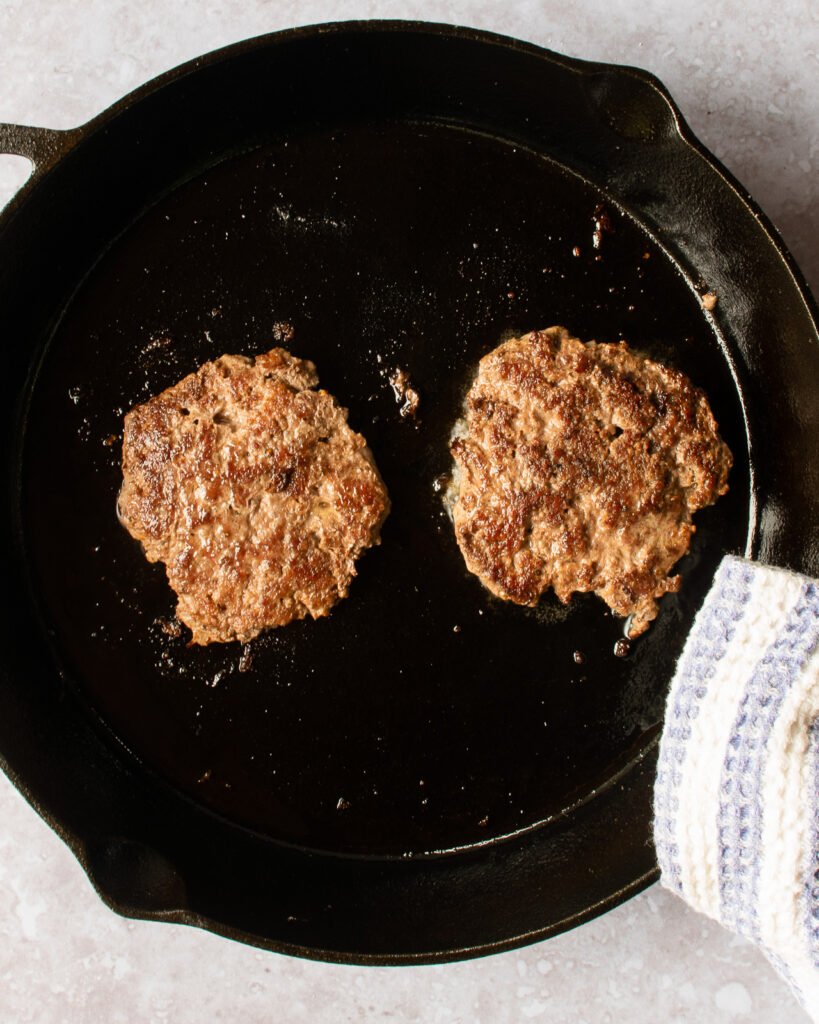 Two cooked smash burgers in a cast iron pan.