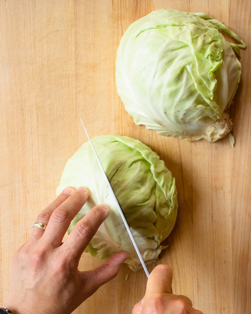 Two hands cutting half a head of cabbage in quarters.