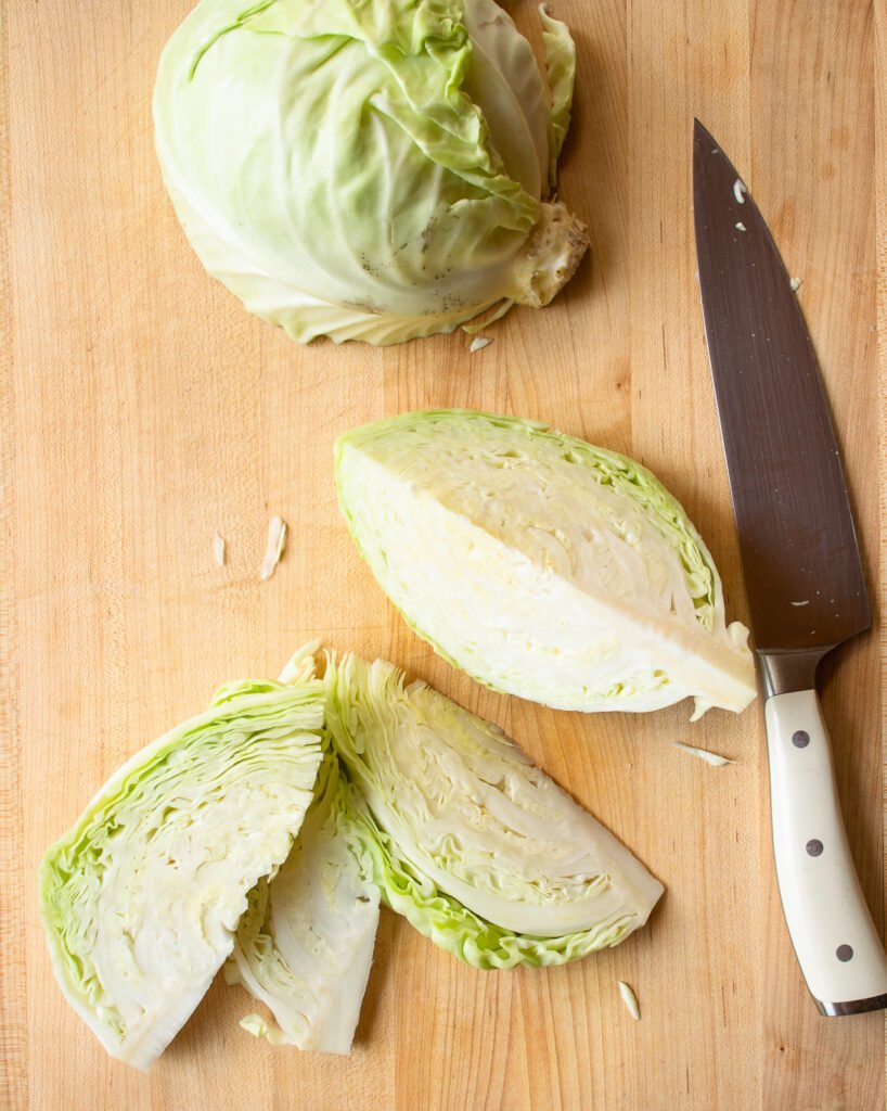 Wedges of green cabbage on a butcher block with a knife.