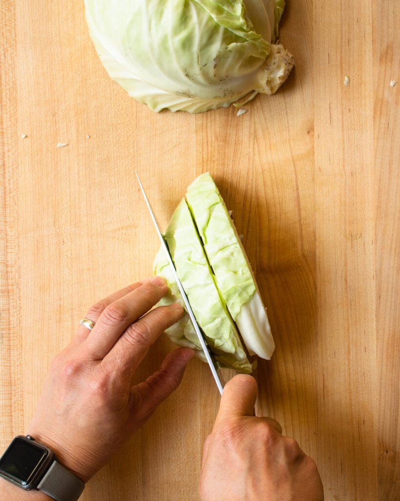 Two hands slicing cabbage wtih a knife.