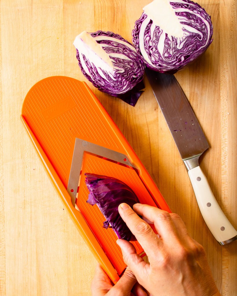 Shredding red cabbage on an orange mandolin.