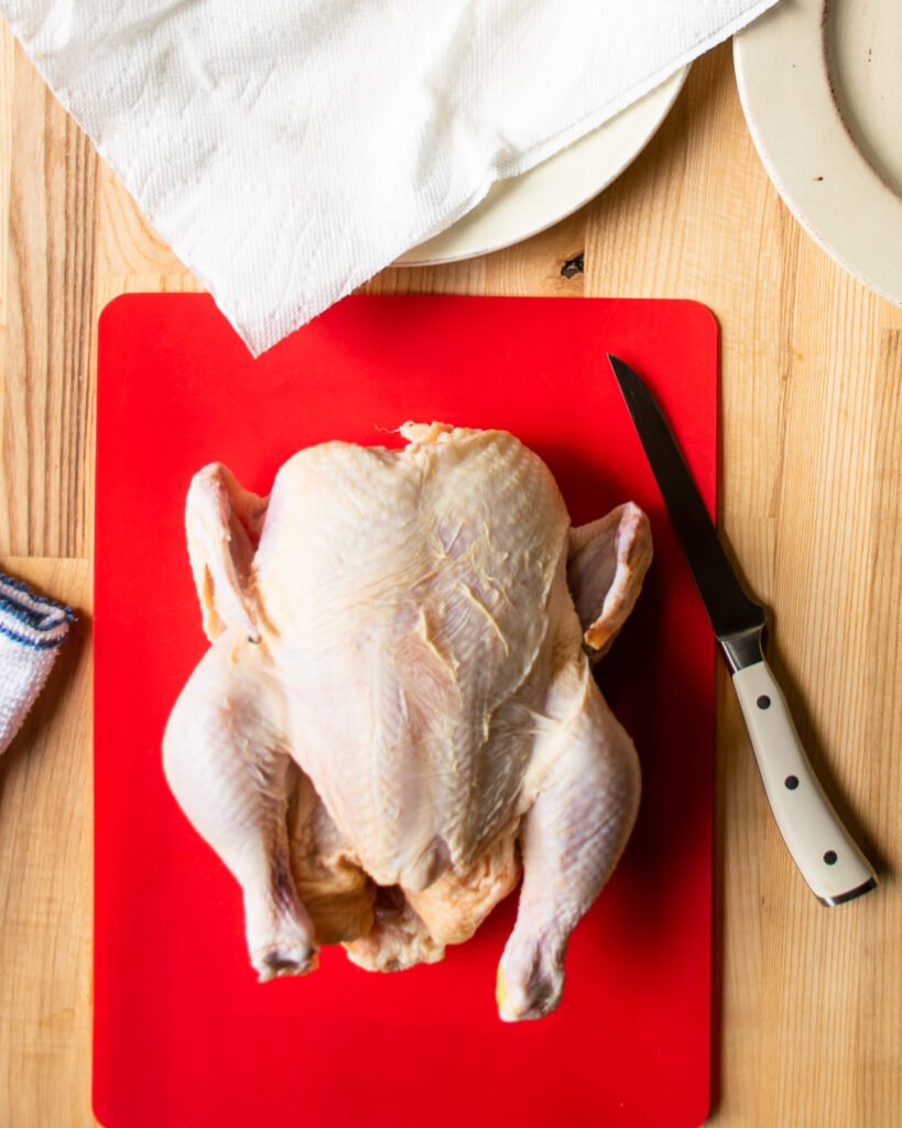A raw chicken on a red cutting board with a boning knife next to it.
