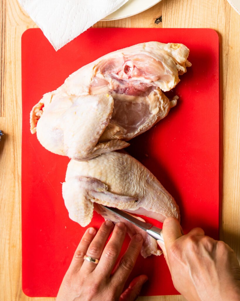 Trimming a chicken split breast on a red cutting board.