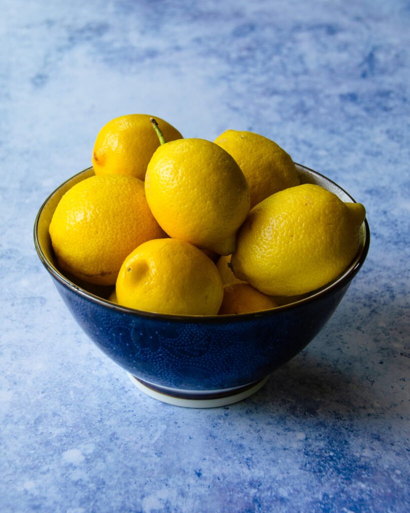 A blue bowl of lemons on a blue marble background.