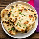 Naan breads on a white plate on a wooden table with pink and purple napkins.