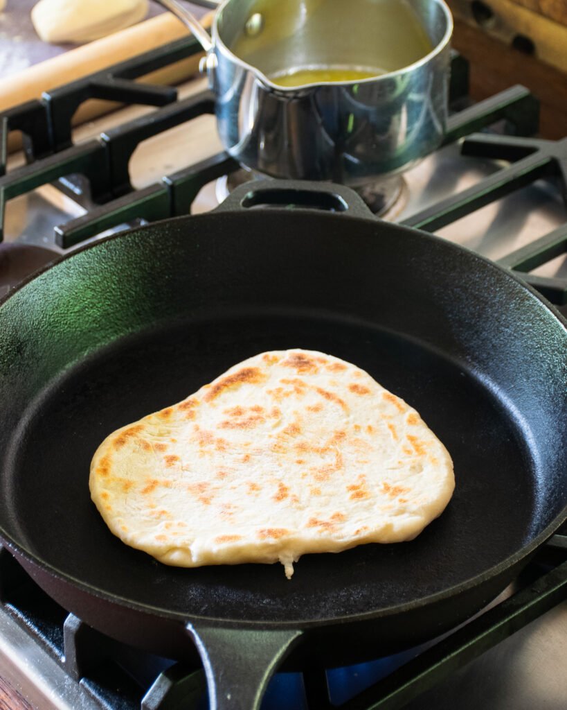 Naan bread in a skillet with one side cooked.