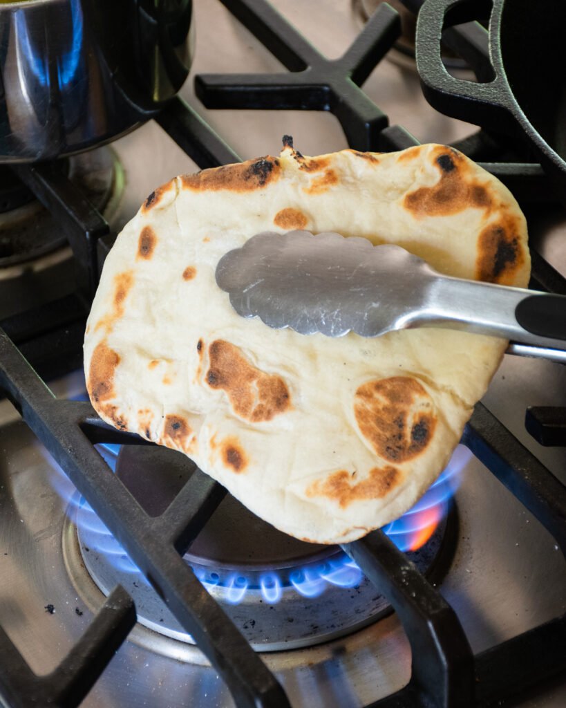 Toasting naan bread over an open gas burner.