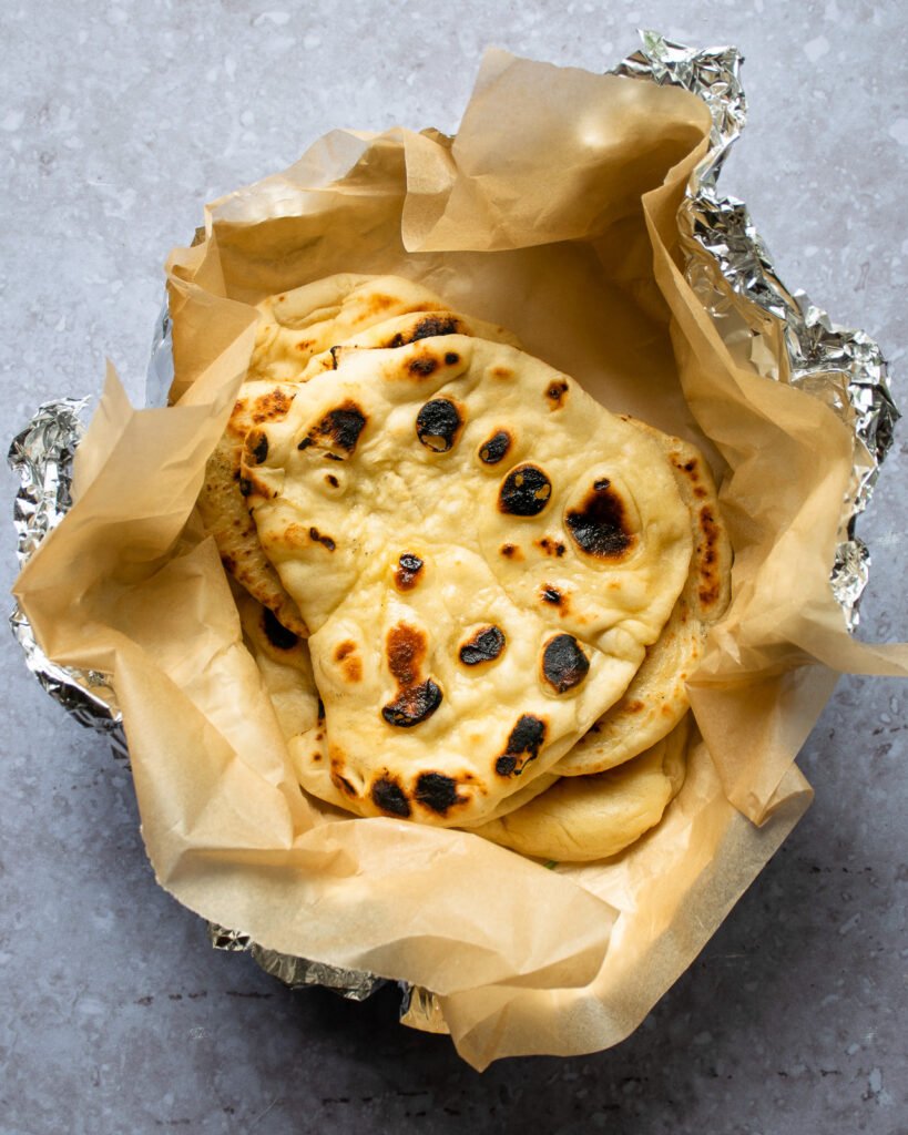 Homemade naan bread in parchment paper and aluminum foil on a counter top.