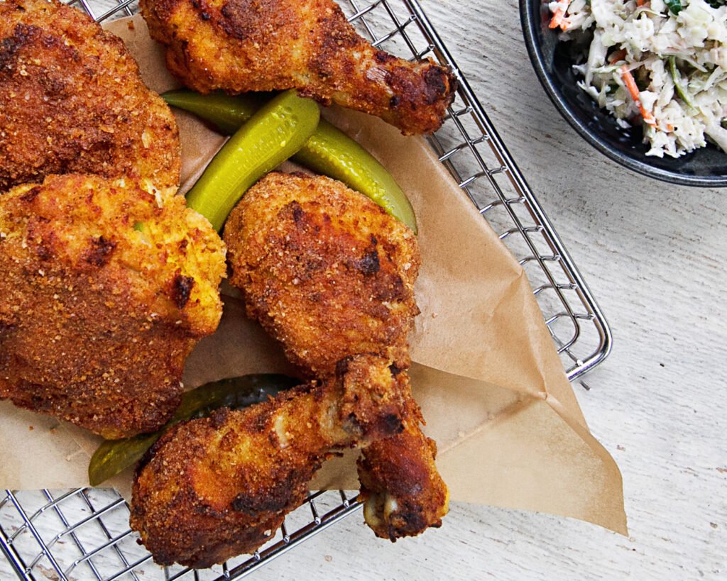 pickle brined fried chicken in a wire basket with a small bowl of coleslaw near by.
