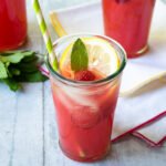A glass of sparkling raspberry lemonade with a green striped straw on a grey wooden table.
