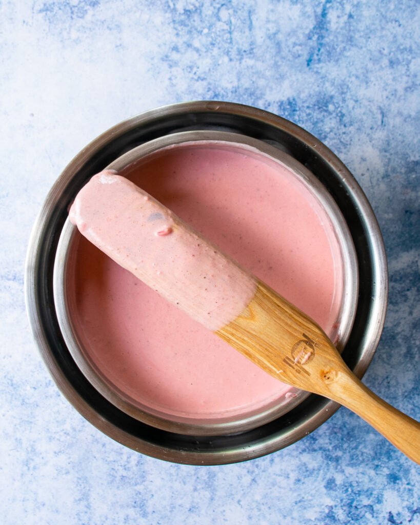 Strawberry Ice Cream base cooling in an ice bath with a wooden spoon resting on the bowl.