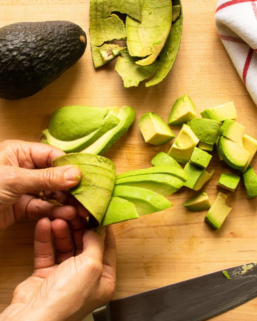 Two hands peeling the skin away from slices of avocado.