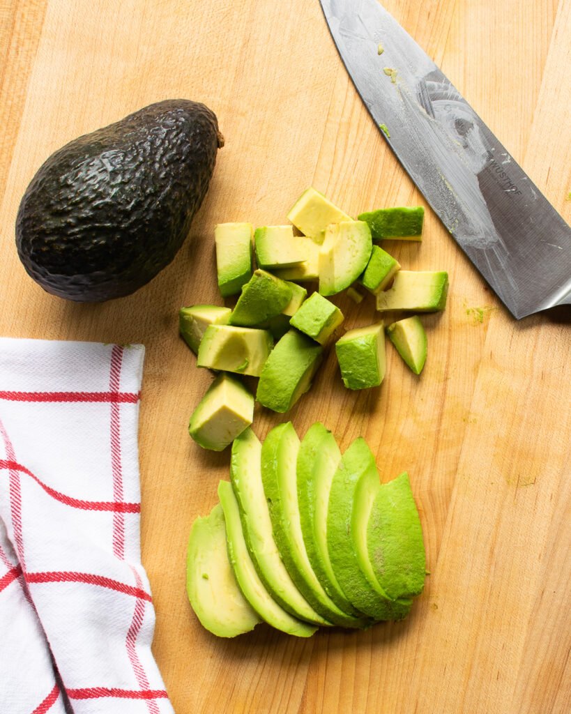 An avocado next to sliced and diced avocado pieces and a chef's knife.