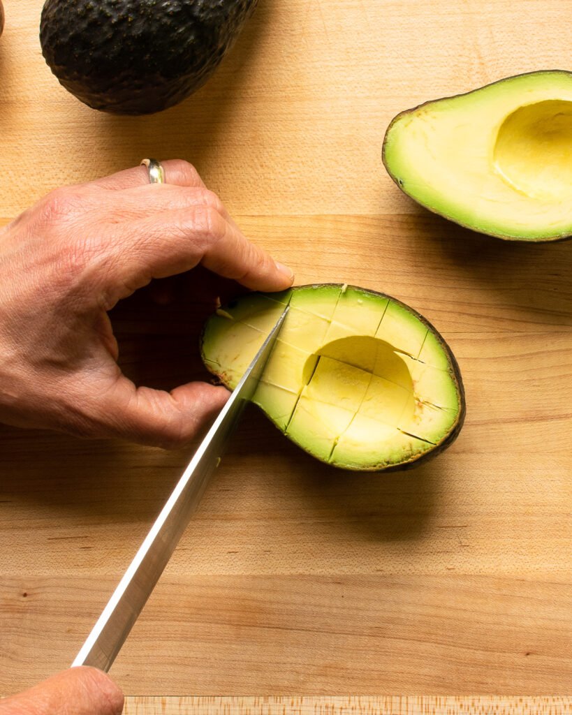 A knife cutting cross hatch marks in half an avocado.