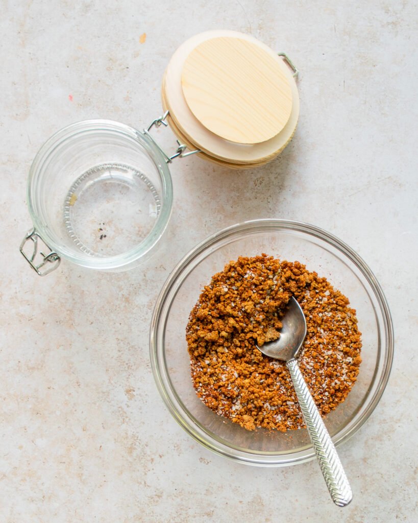 Best dry rub spice mix in a glass bowl with a spoon and an empty glass jar next to it.