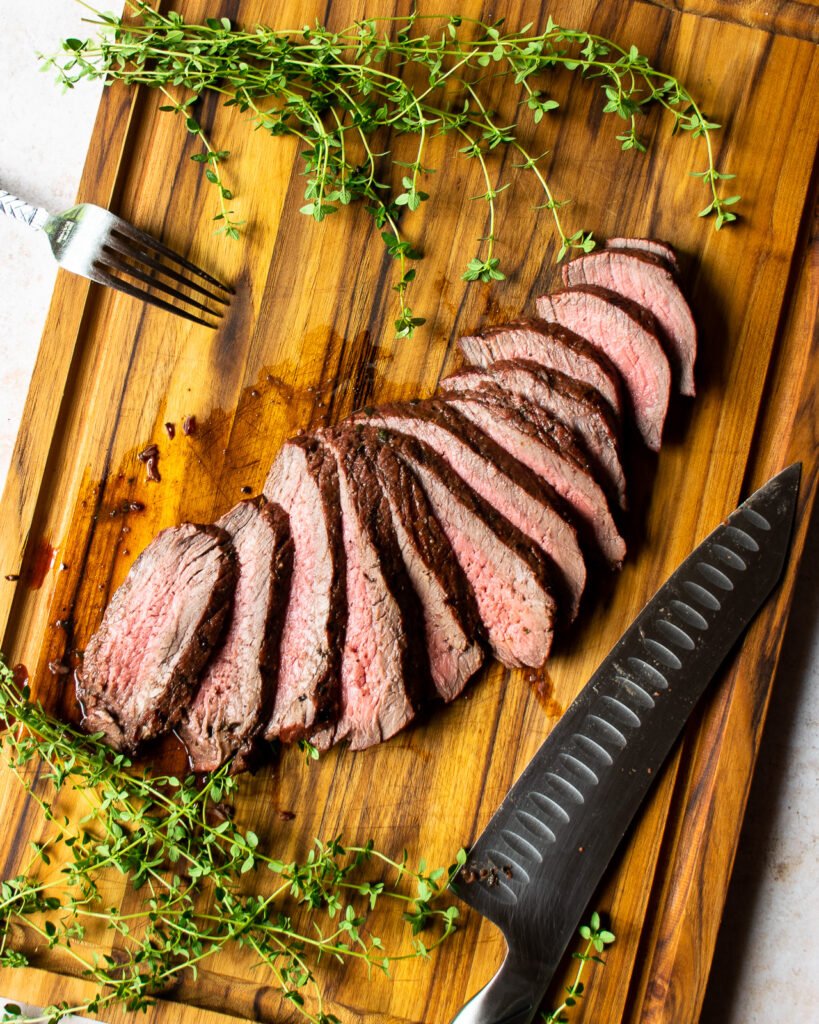 Grilled Marinated London Broil sliced on a cutting board with a slicing knife and fresh thyme.