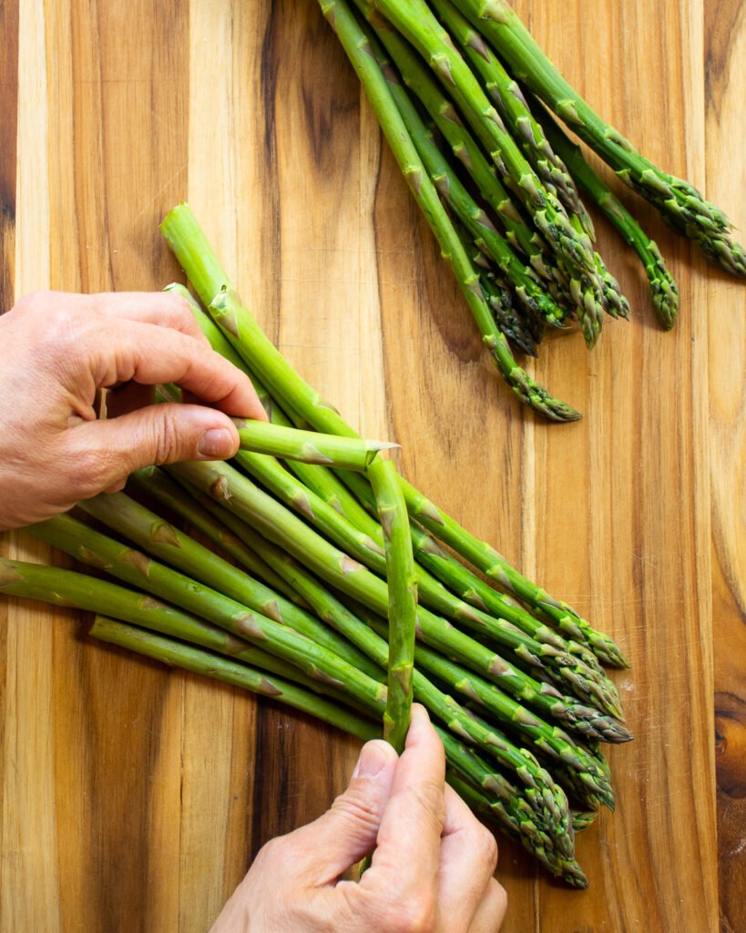 Hands breaking a spear of asparagus over a cutting board.