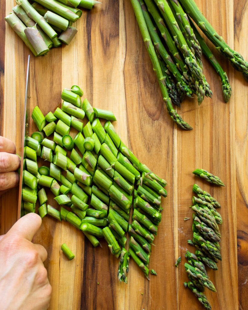 Asparagus chopped on a wooden cutting board.