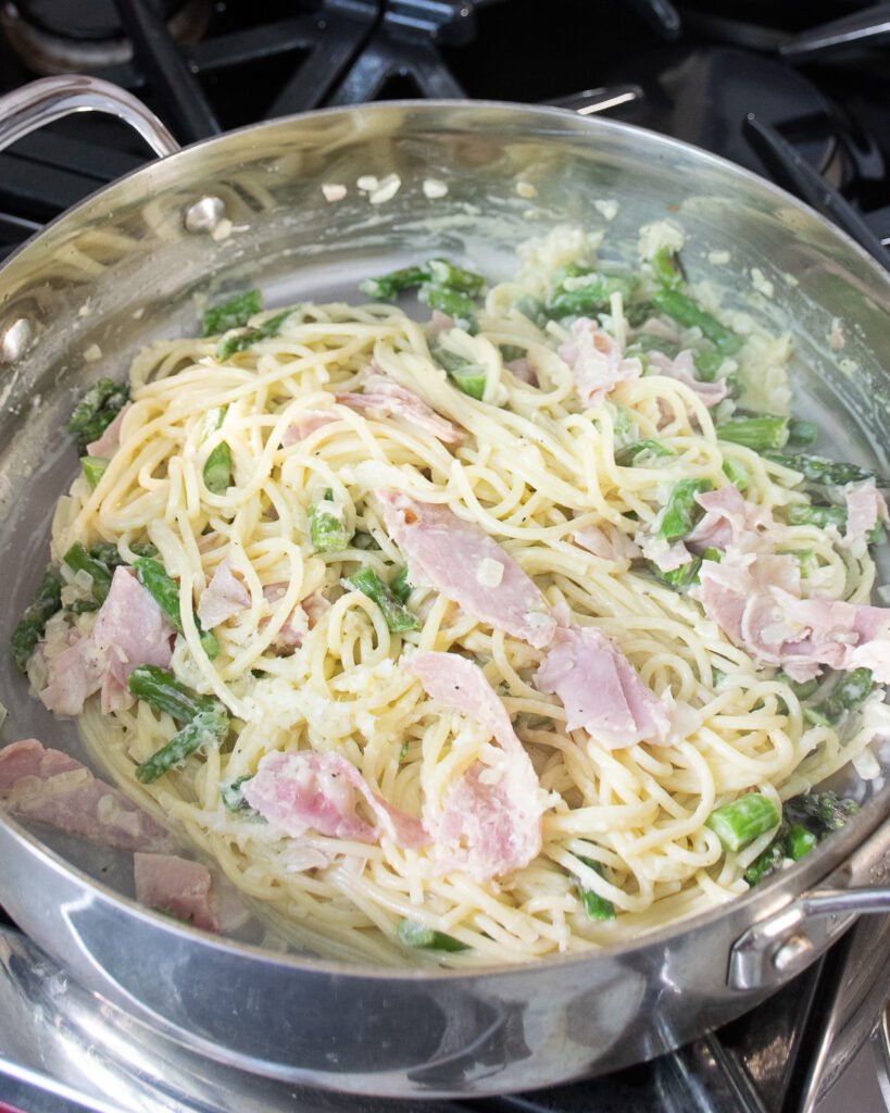 Creamy ham and asparagus pasta in a large stainless steel skillet