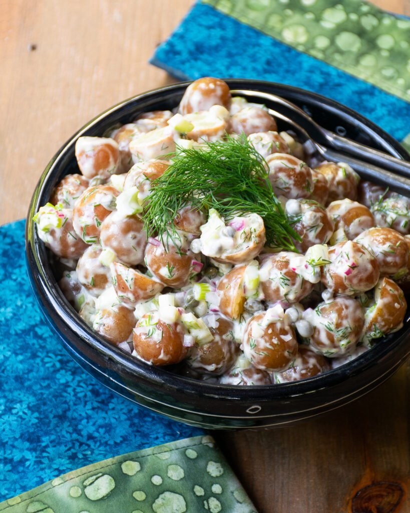 Instant Potato Salad with Lemon Mayo in a black bowl on a wooden table with blue and green napkins.