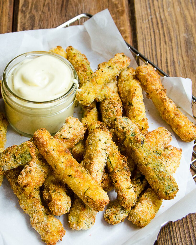 Zucchini fries in a paper-lined wire basket with a dipping sauce.