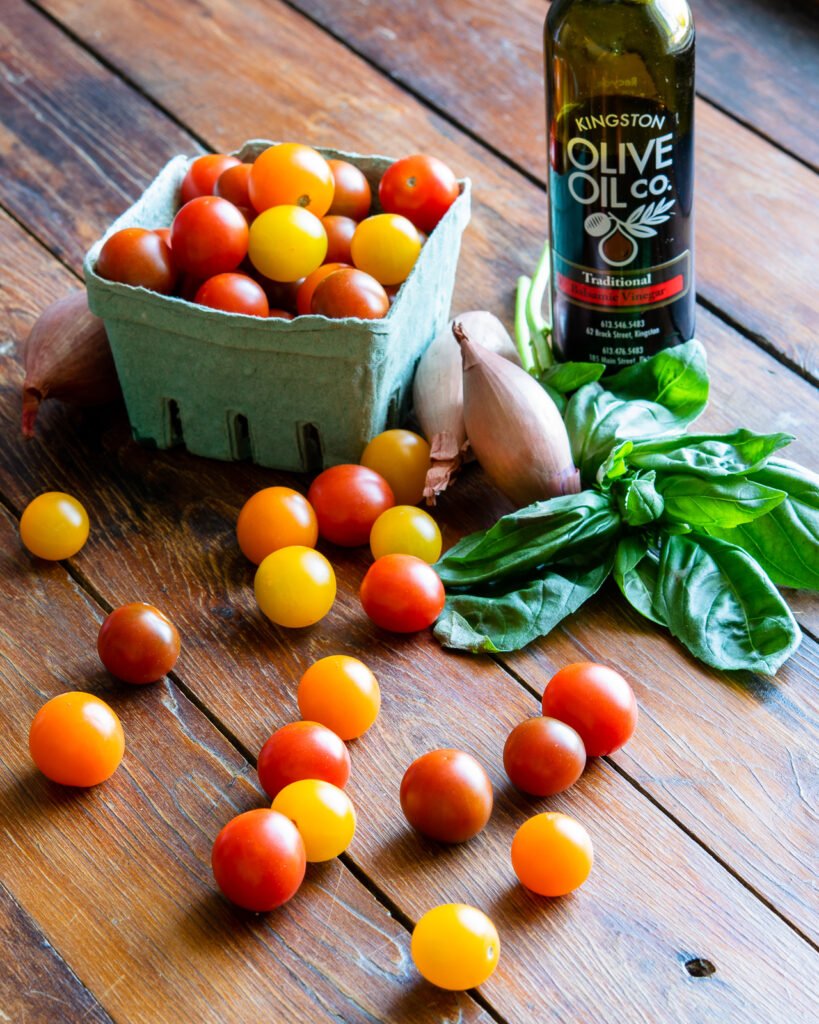 Cherry tomatoes in a cardboard pint container, shallots, basil, balsamic vinegar on a wooden table.