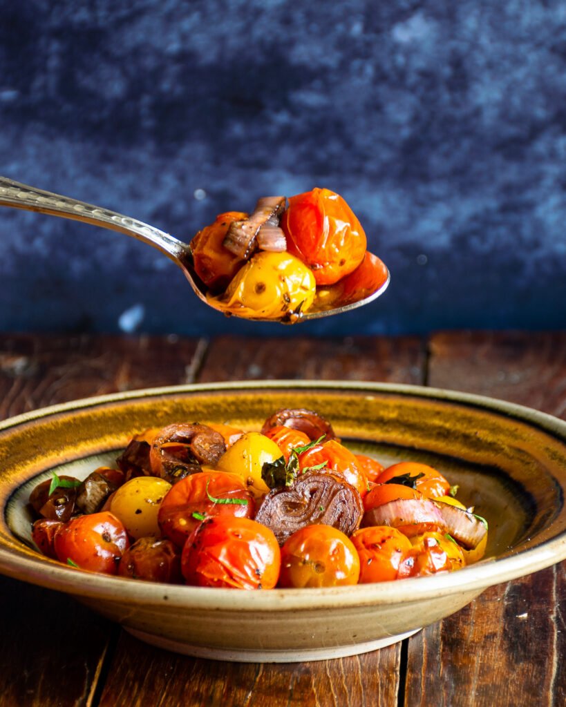 Roasted cherry tomatoes being lifted out of a bowl with a spoon.