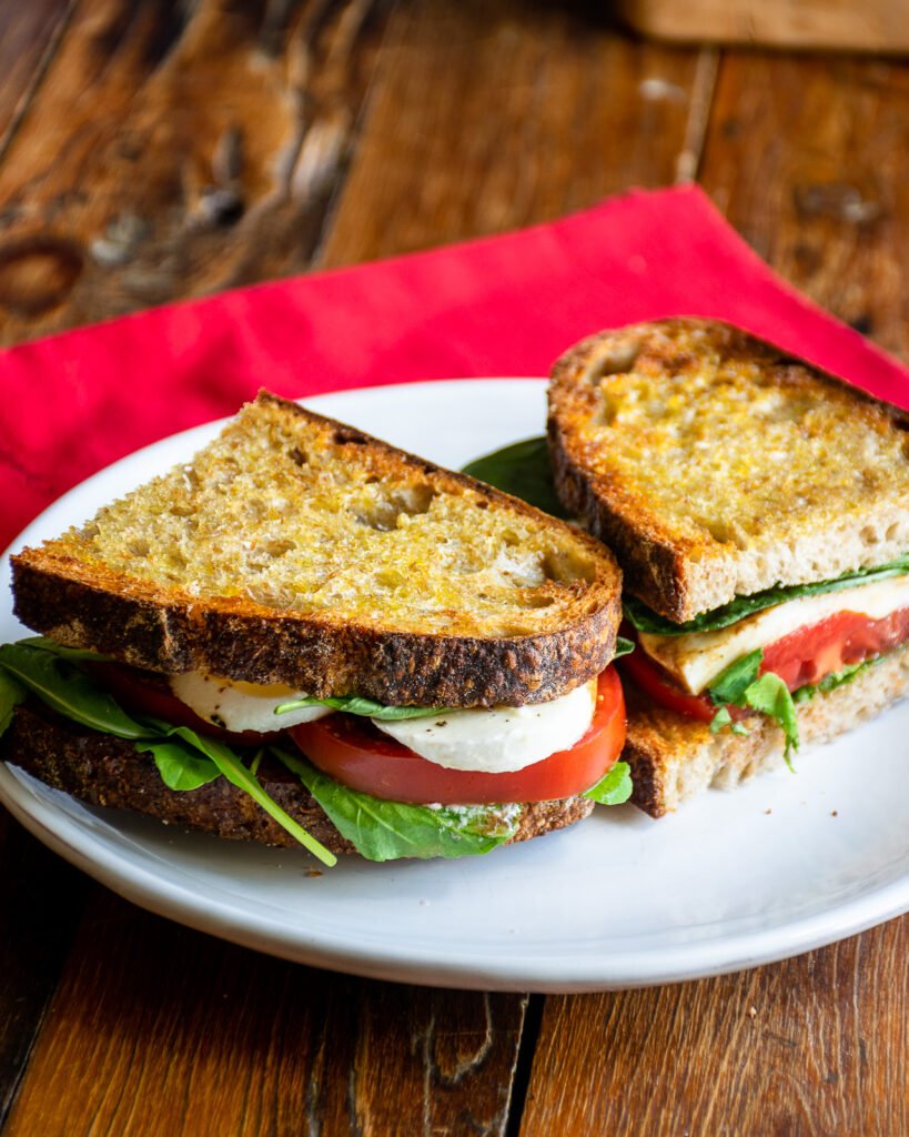 A caprese sandwich on a white plate with a red napkin in the background.