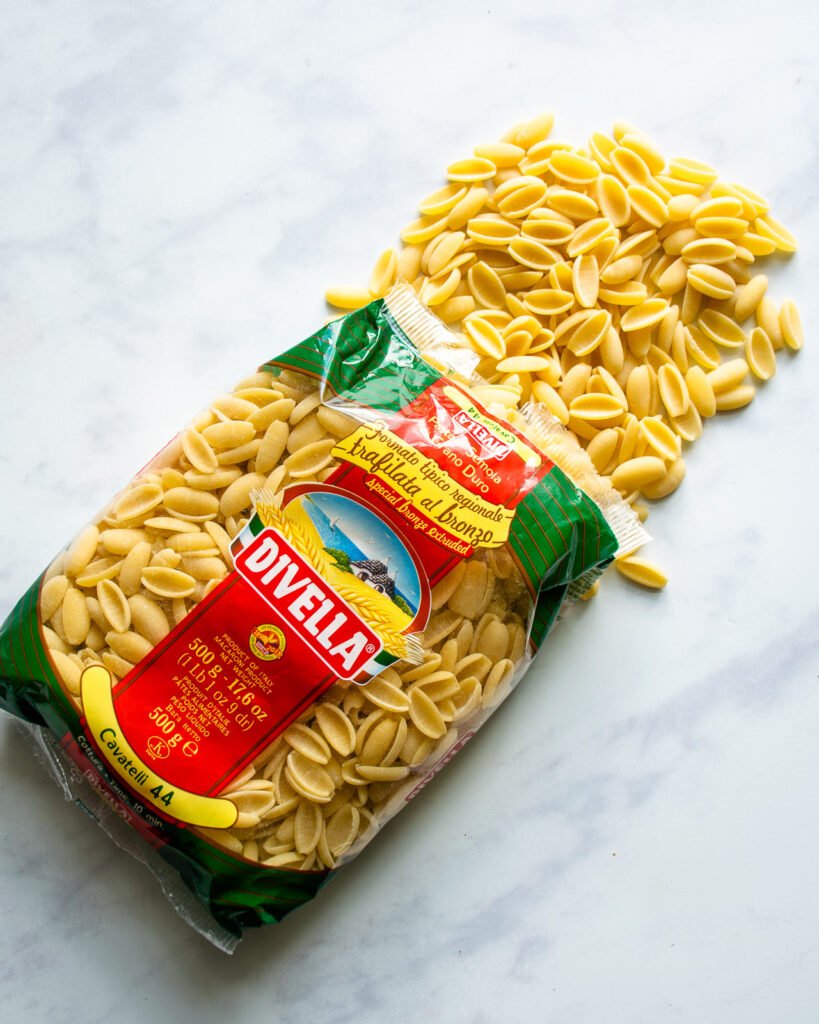 Cavatelli pasta spilling out of a bag on a marble counter.