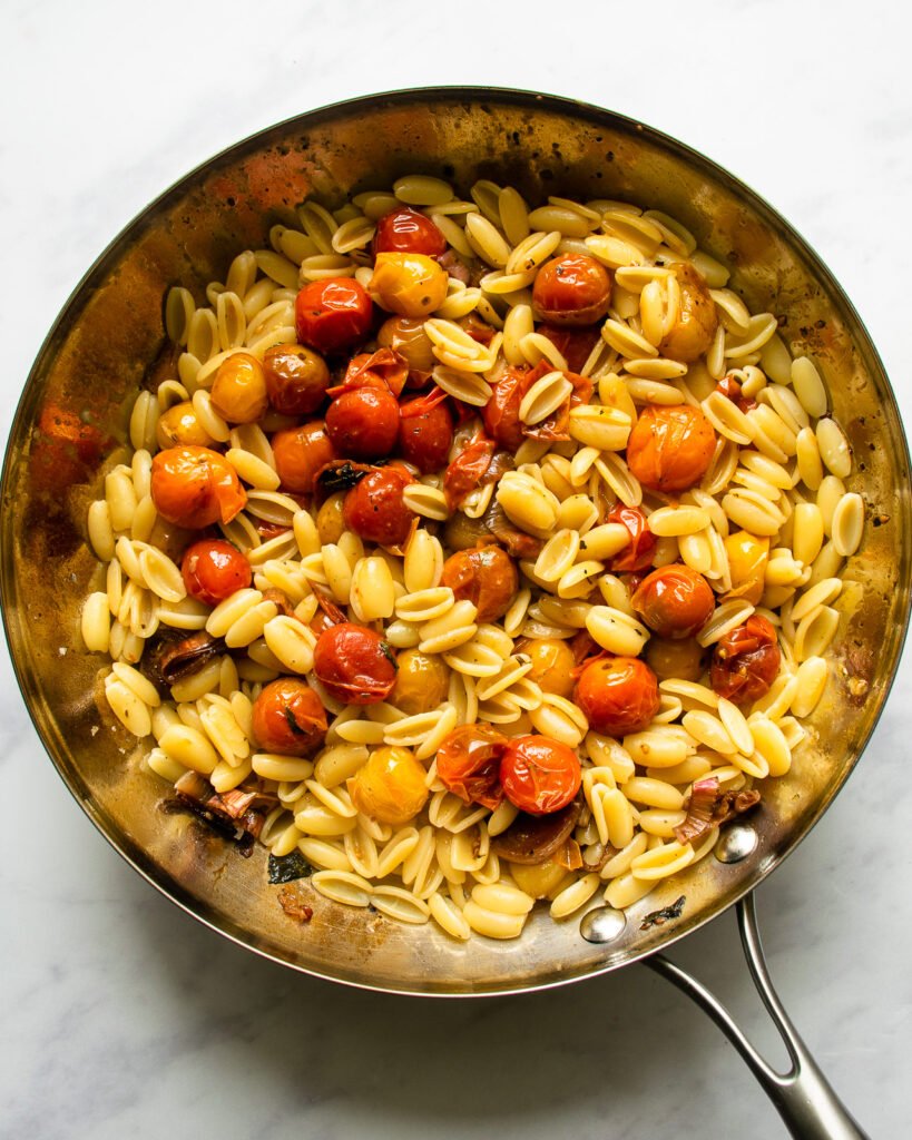 Cavatelli pasta with cherry tomatoes and pancetta in a skillet.
