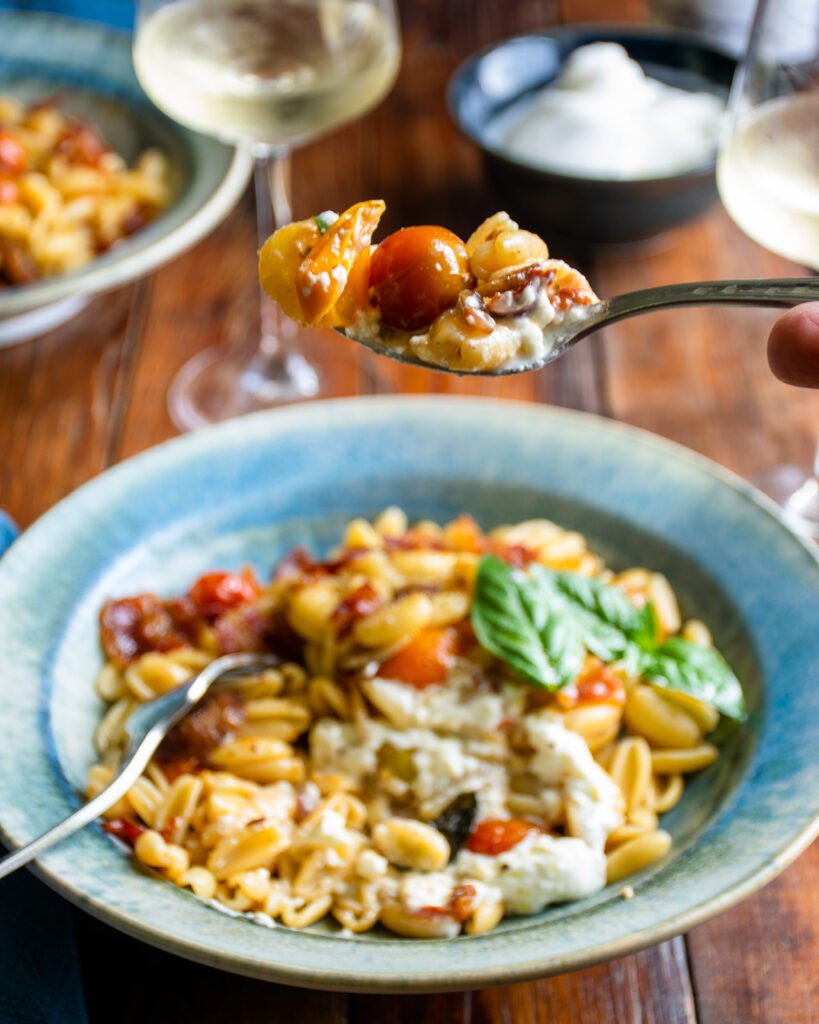 A spoon lifting cavatelli with roasted cherry tomatoes out of a bowl.