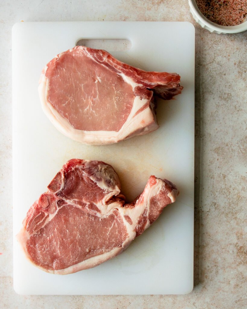 Two pork chops on a white cutting board.