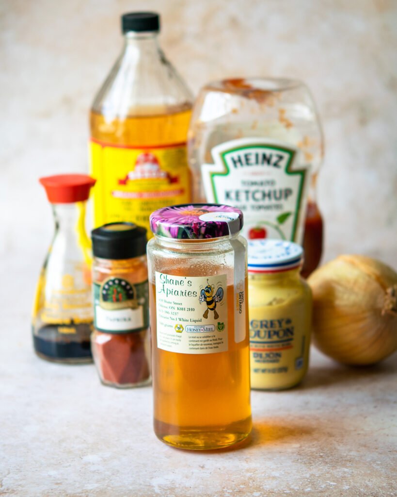 Ingredients on a counter - honey, paprika, soy sauce, cider vinegar, ketchup, mustard and an onion.