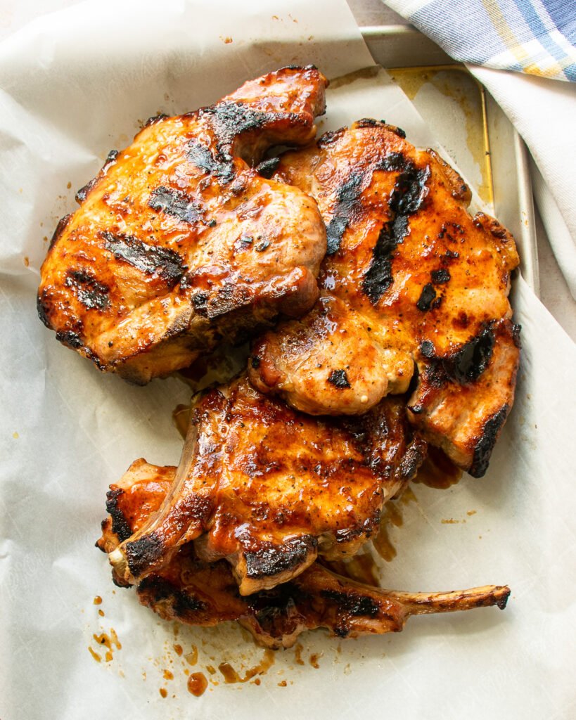 grilled pork chops on a parchment paper-lined baking tray.