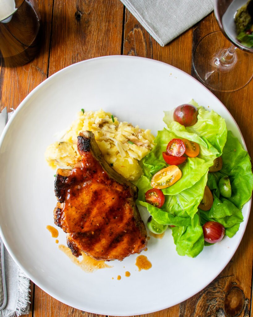 Honey BBQ Grilled Pork chop on a white dinner plate with mashed potatoes and salad.