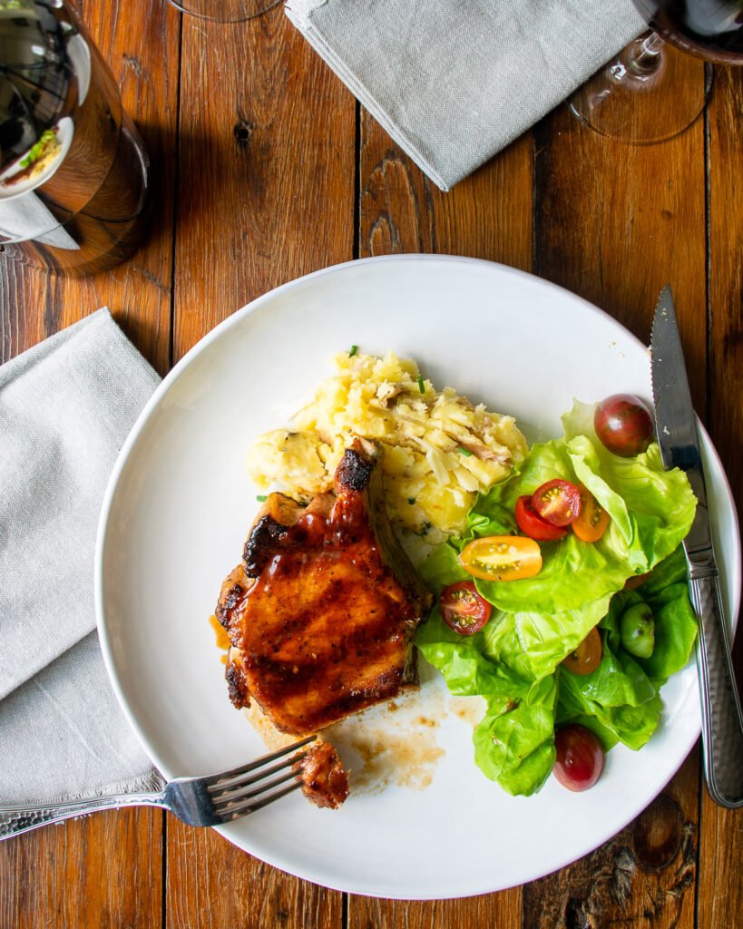 A meal on a white dinner plate with mashed potatoes and salad with wine and napkins.