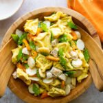 Sesame Chicken Tortellini Salad in a wooden bowl with servers on a table with an orange kitchen towel.