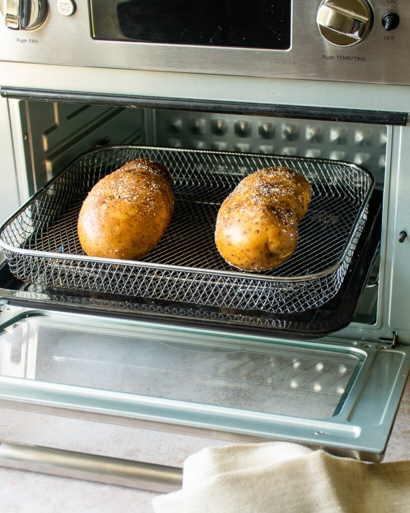 Two potatoes baking in an air fryer oven.