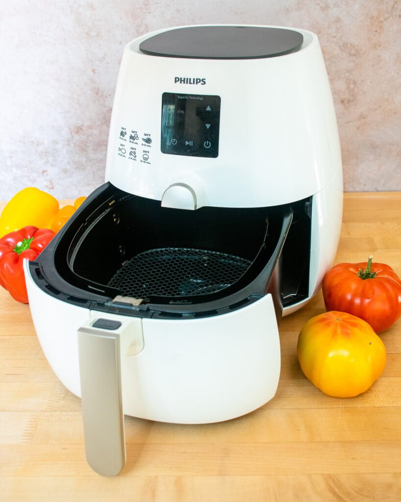 A white air fryer with the drawer partially pulled out on a butcher block counter.