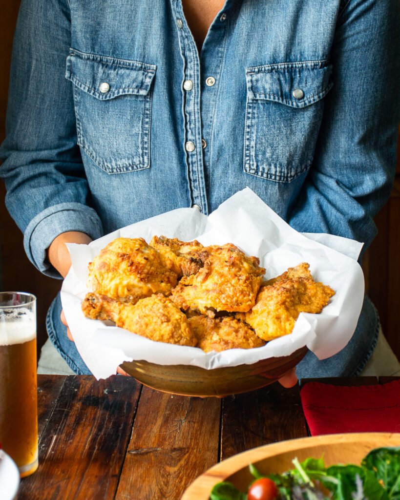 Air Fryer fried chicken being presented by someone in a parchment lined basket.