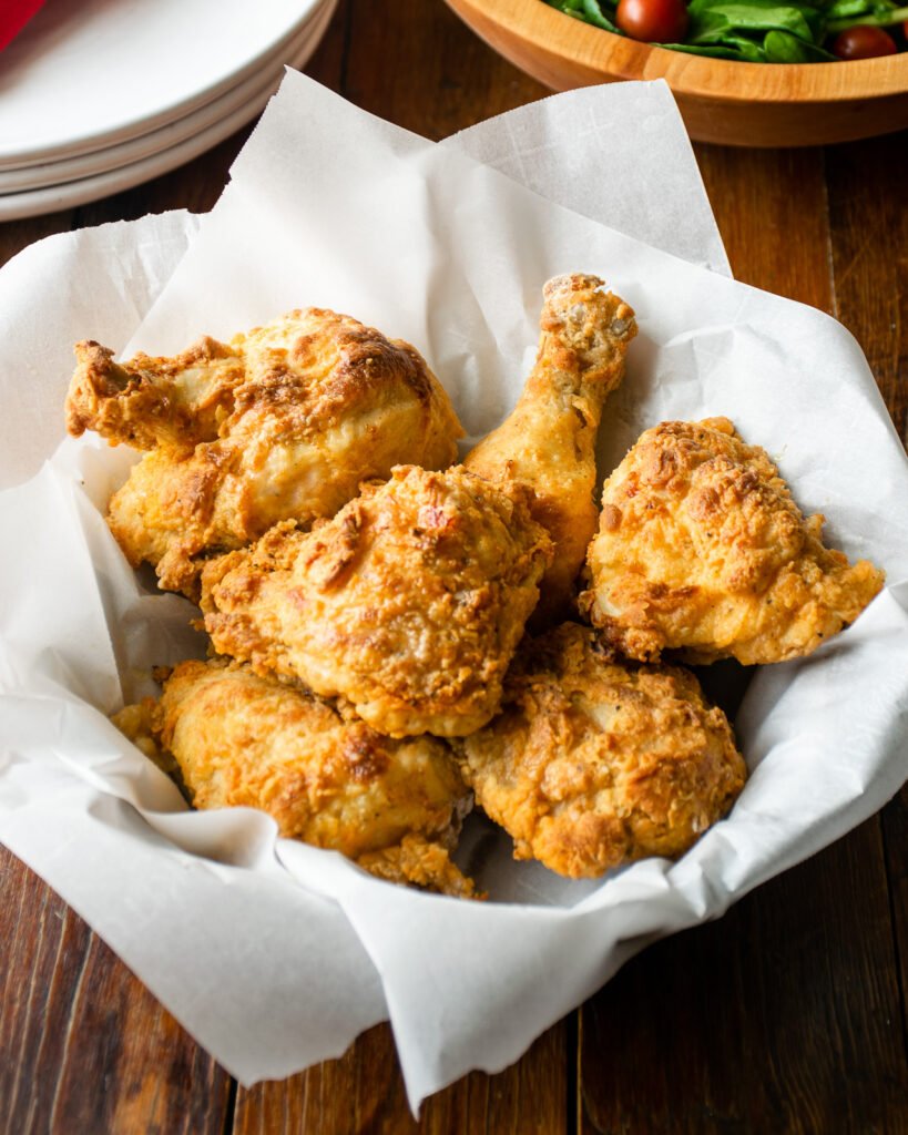 Buttermilk air fried fried chicken in a parchment paper lined basket on a wooden table.
