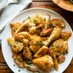 Apple Cider Glazed Chicken on a white plate with a bowl of salad and serving utensils.