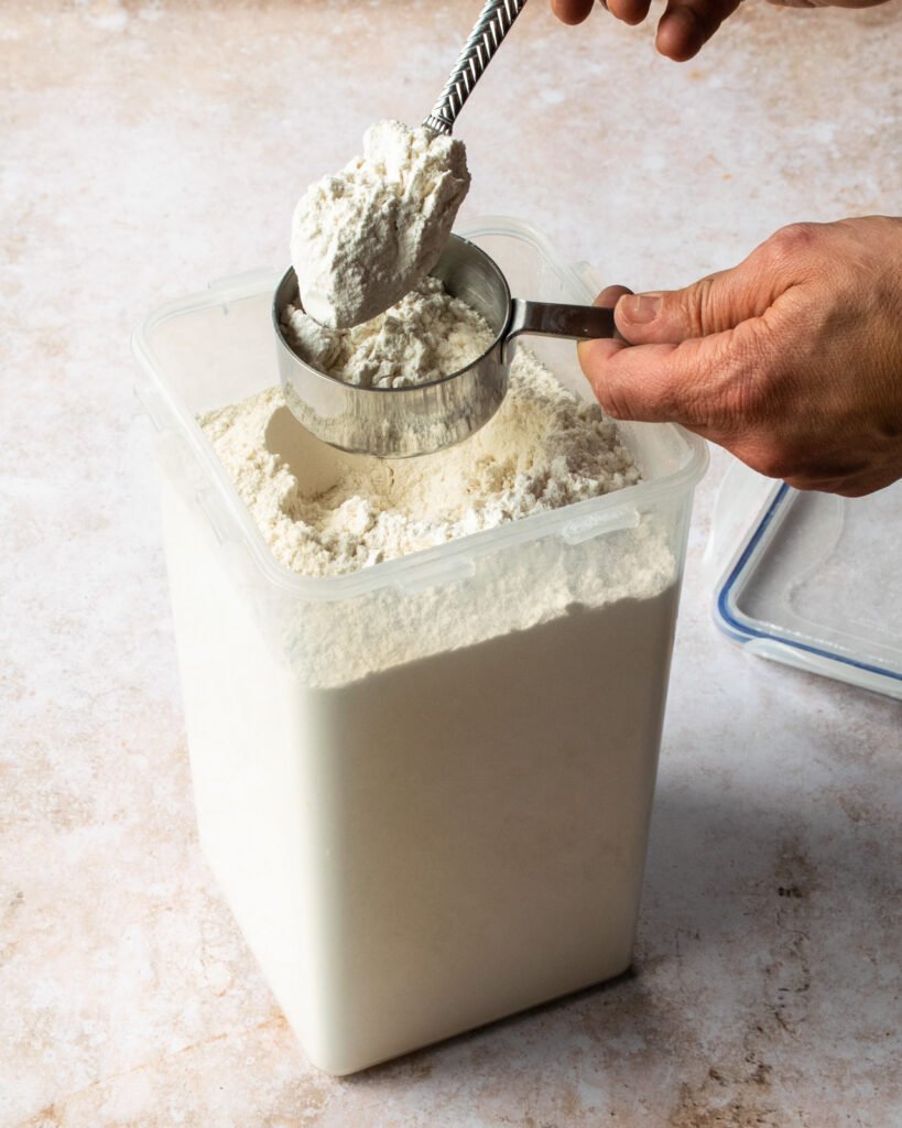 Two hands spooning flour into a dry cup measure.